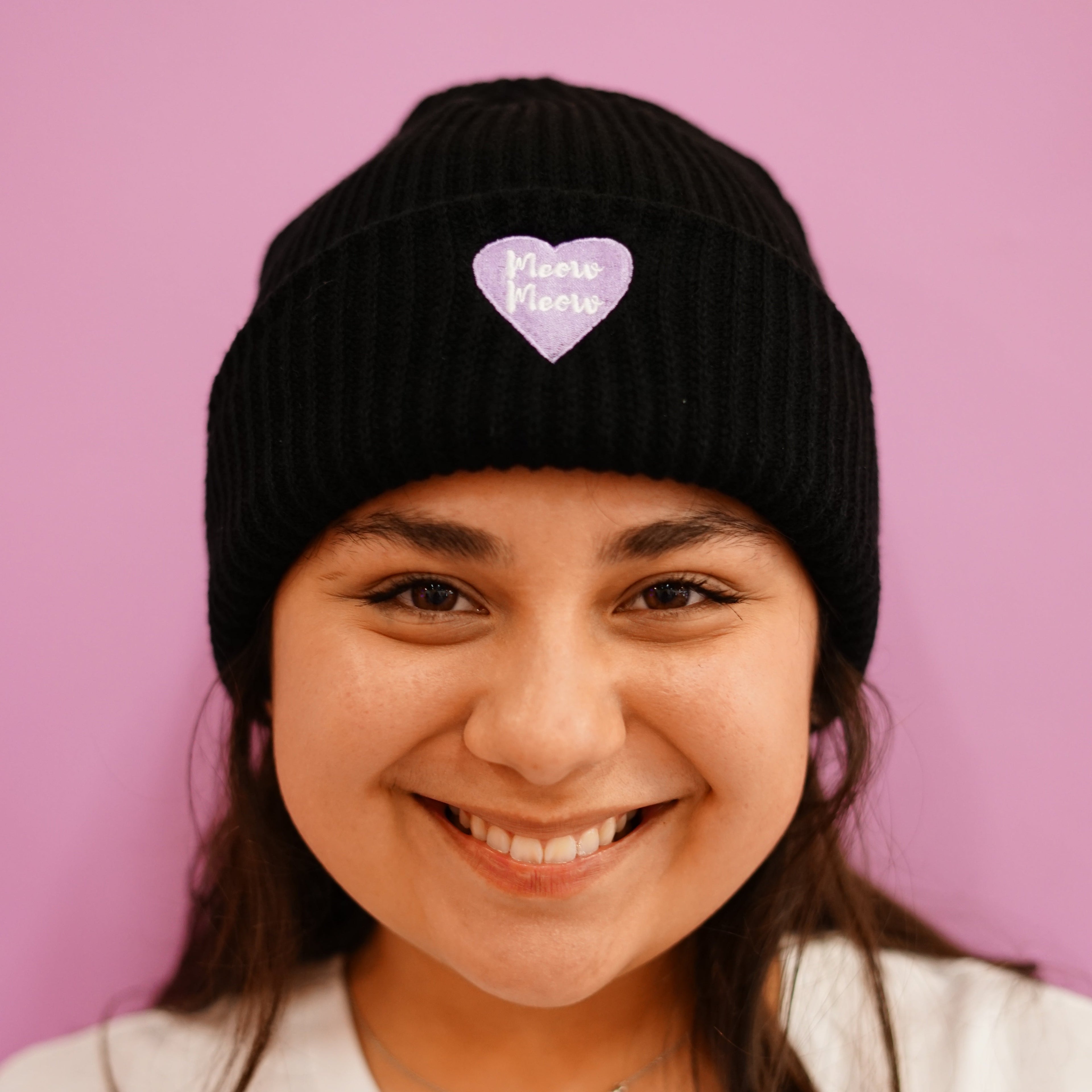 Person wearing a black beanie with a heart design on a pink background